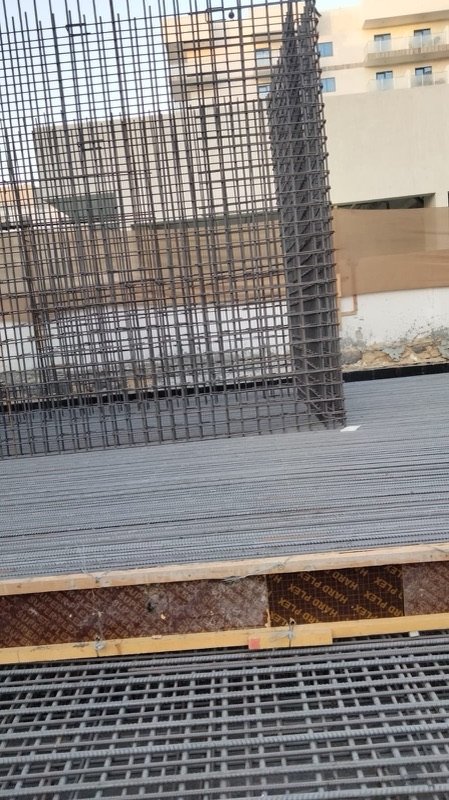 Wall reinforcement cage rising from a raft mat beside timber formwork